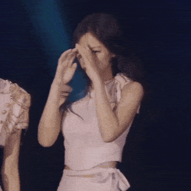 a woman in a white top is covering her face with her hands .