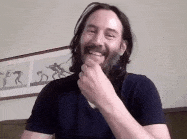 a man with long hair and a beard is laughing while covering his mouth with his hand .