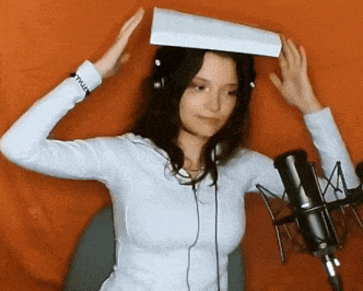 a woman wearing headphones is holding a piece of paper on her head in front of a microphone
