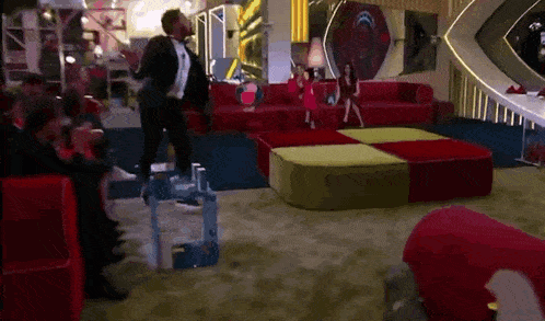 a man in a tuxedo is dancing in a living room with a group of people watching .