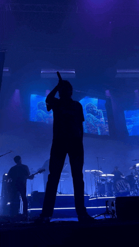 a man singing into a microphone on a stage in front of a large screen with a picture of a person on it