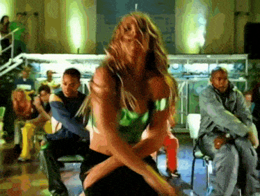 a woman in a green top and black skirt is dancing in front of a crowd