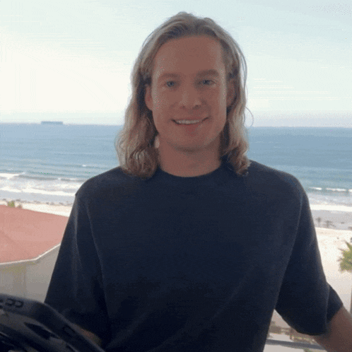 a man with long blonde hair wearing a black shirt with the letter cc on it