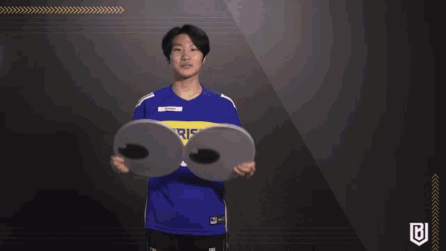 a person wearing a blue and yellow uprising jersey holds up a pair of googly eyes