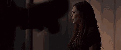a woman in a black jacket is standing in a dark room holding a cell phone .