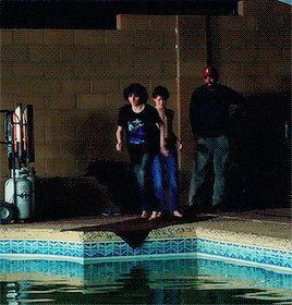 a couple of people standing next to a swimming pool with a propane tank in the background