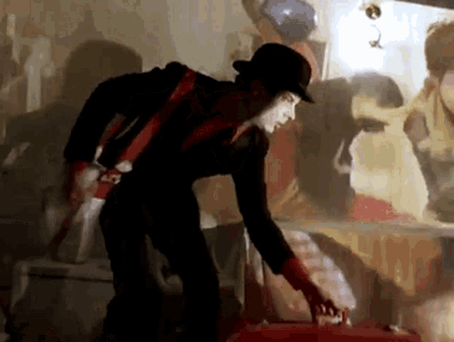 a man wearing a top hat and red gloves is reaching into a red suitcase .