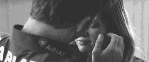 a man and a woman are kissing in a black and white photo . the woman is wearing a ariat shirt .