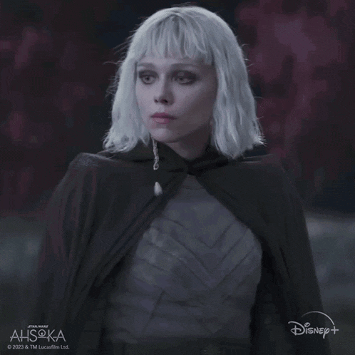 a woman with white hair is wearing a black cape with disney + written on the bottom