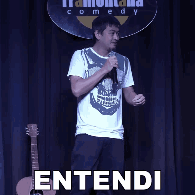 a man holding a microphone in front of a sign that says comedy