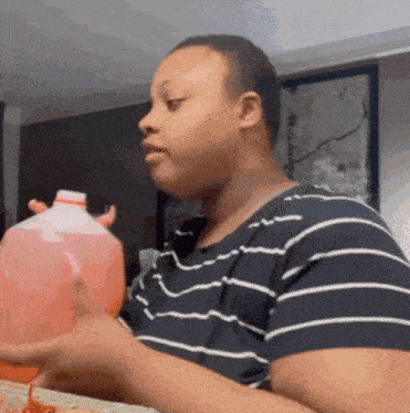 a woman in a striped shirt is holding a bottle of pink liquid .