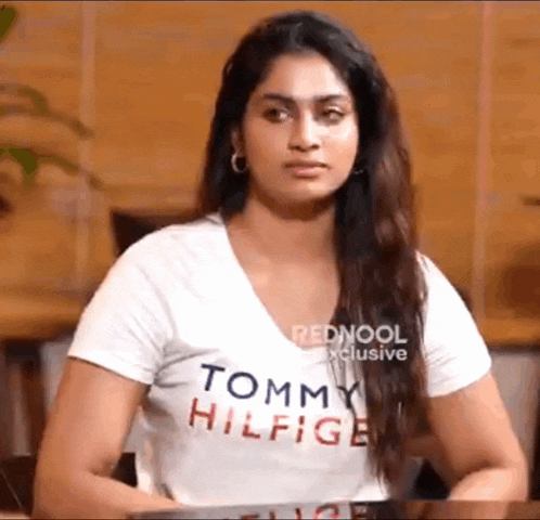 a woman in a white tommy hilfiger t-shirt is sitting at a table .