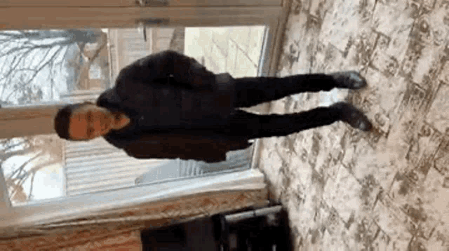 a man in a black jacket is standing in a living room in front of a glass door .