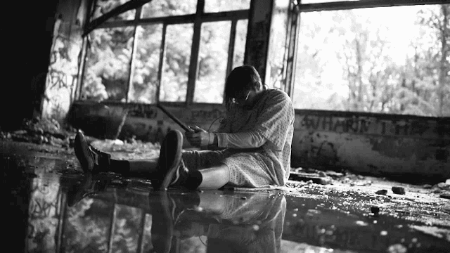 a black and white photo of a person sitting in a puddle with graffiti on the wall