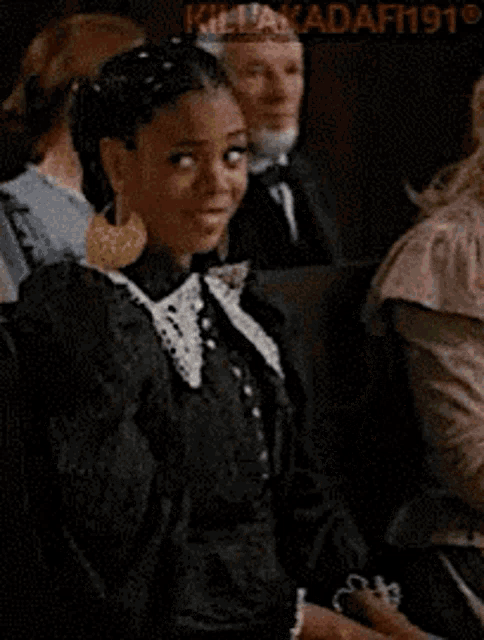 a woman in a black dress is standing in front of a crowd and says you and me .