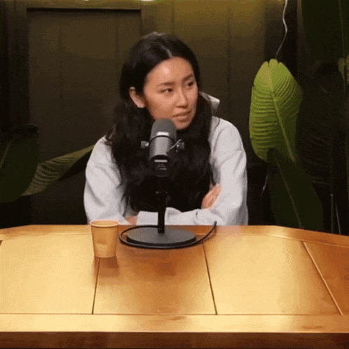 a woman sits at a table with a microphone and a cup