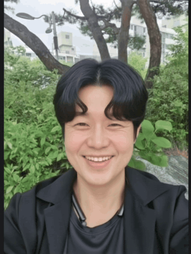 a man in a black jacket is smiling in front of trees