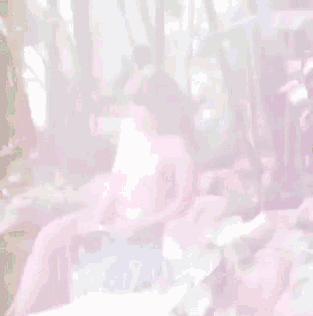 a blurry picture of a woman in a pink dress sitting in the woods