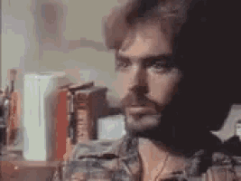 a man with a beard is looking at himself in a mirror in a room .