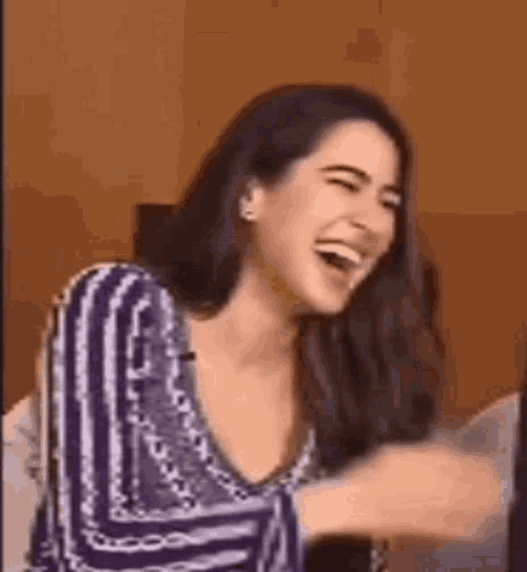 a woman is laughing with her mouth open while wearing a purple and white striped shirt .