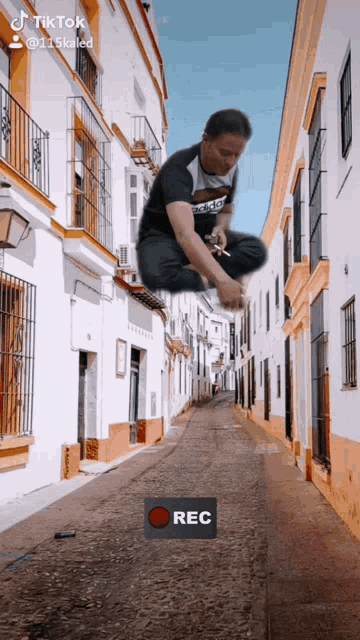 a man is jumping in the air on a street with a red rec button in the corner