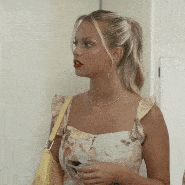 a blonde woman wearing a floral dress and a yellow bag
