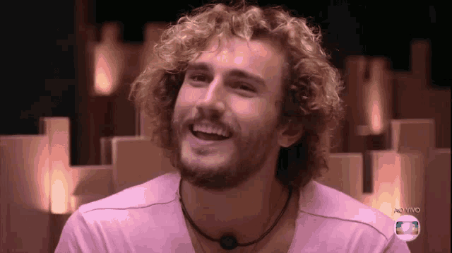 a man with curly hair and a beard is smiling in a pink shirt
