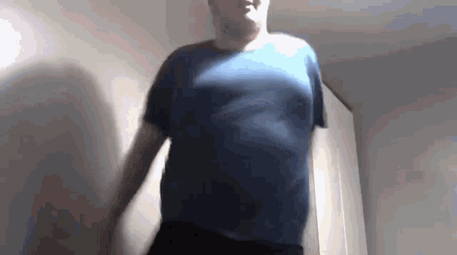 a man in a blue shirt is standing in a room with his arms outstretched .