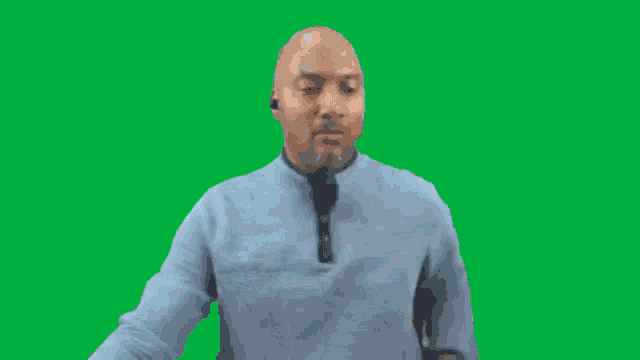 a bald man wearing a blue sweater and ear buds is standing on a green screen .