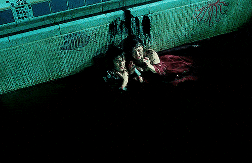 two people are swimming in a pool with a fish and octopus painted on the wall behind them