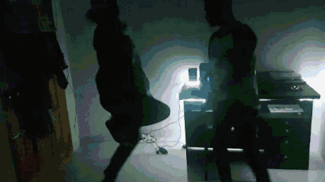 two people are dancing in a dark room with a desk in the background