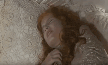 a woman with red hair is laying on a bed with her eyes closed and a white blanket .
