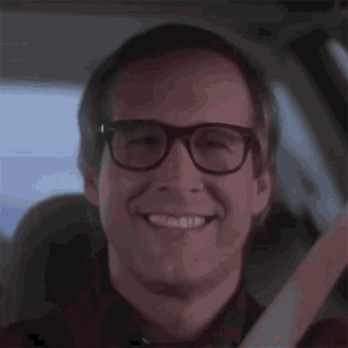 a man wearing glasses is smiling while sitting in the driver 's seat of a car