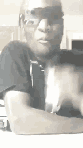 a man wearing sunglasses and a mask is sitting at a table with his hands folded .