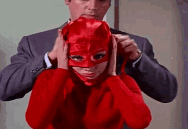 a man is helping a woman put on a red mask .