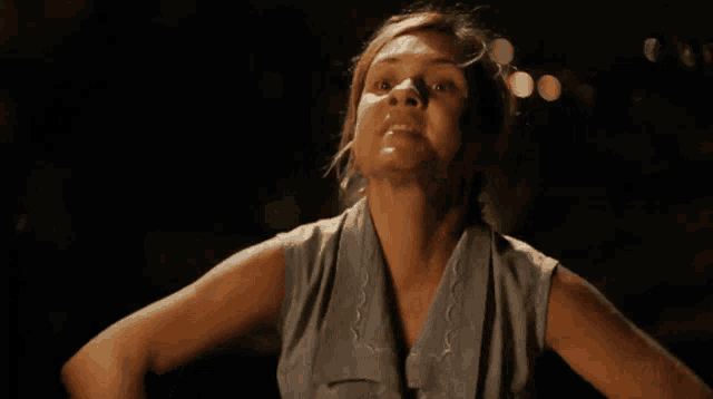 a woman in a blue tank top is standing in the dark with her arms outstretched