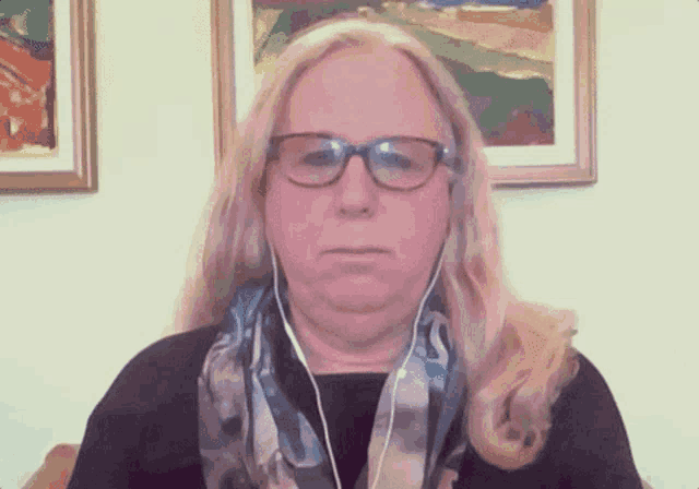 a woman wearing glasses and a scarf is sitting in front of paintings