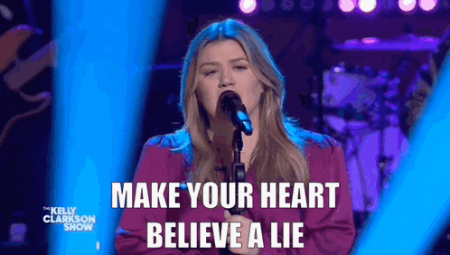 a woman singing into a microphone with the words " make your heart believe a lie " behind her