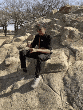 a man is sitting on a rock wearing sunglasses and a black shirt
