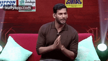 a man is sitting on a red couch with his hands folded in prayer .
