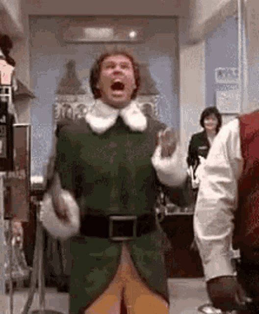 a man dressed as a christmas elf is standing in a hallway with his mouth open .