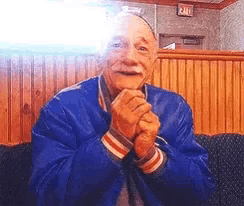 an elderly man in a blue jacket is sitting on a couch with his hands folded