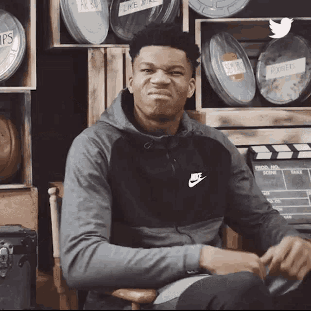 a man wearing a nike hoodie is sitting in front of a clapper board