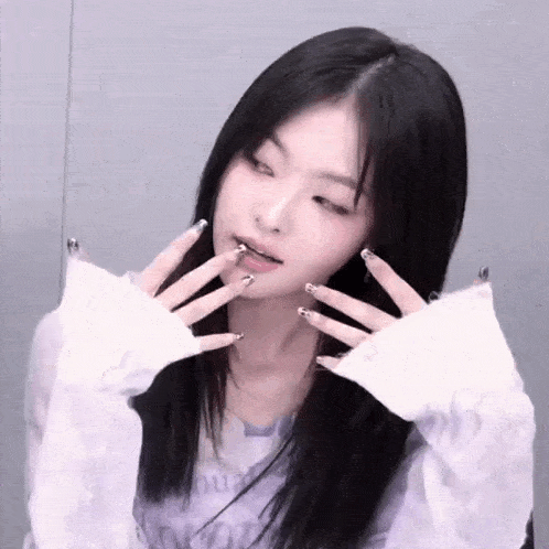a woman with long black hair and long nails is wearing a white sweater and making a funny face .