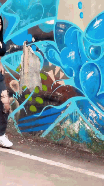 a woman is standing in front of a wall that has graffiti on it
