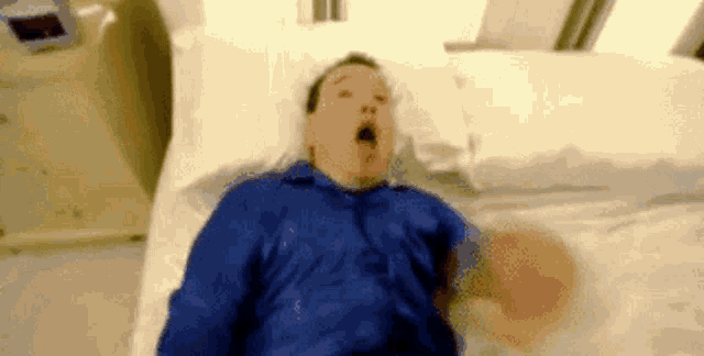 a man in a blue shirt is laying on a hospital bed with his mouth open .