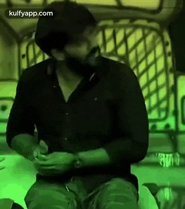 a man with a beard is sitting on a chair in a dark room with a green background .