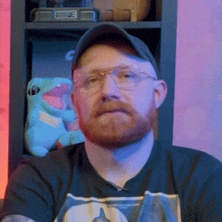 a man with a beard wearing glasses and a baseball cap looks at the camera
