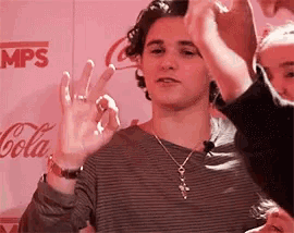 a man wearing a necklace and a watch is giving the ok sign while standing in front of a coca cola sign .