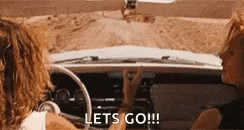 two women are driving a car on a dirt road and they are talking to each other .